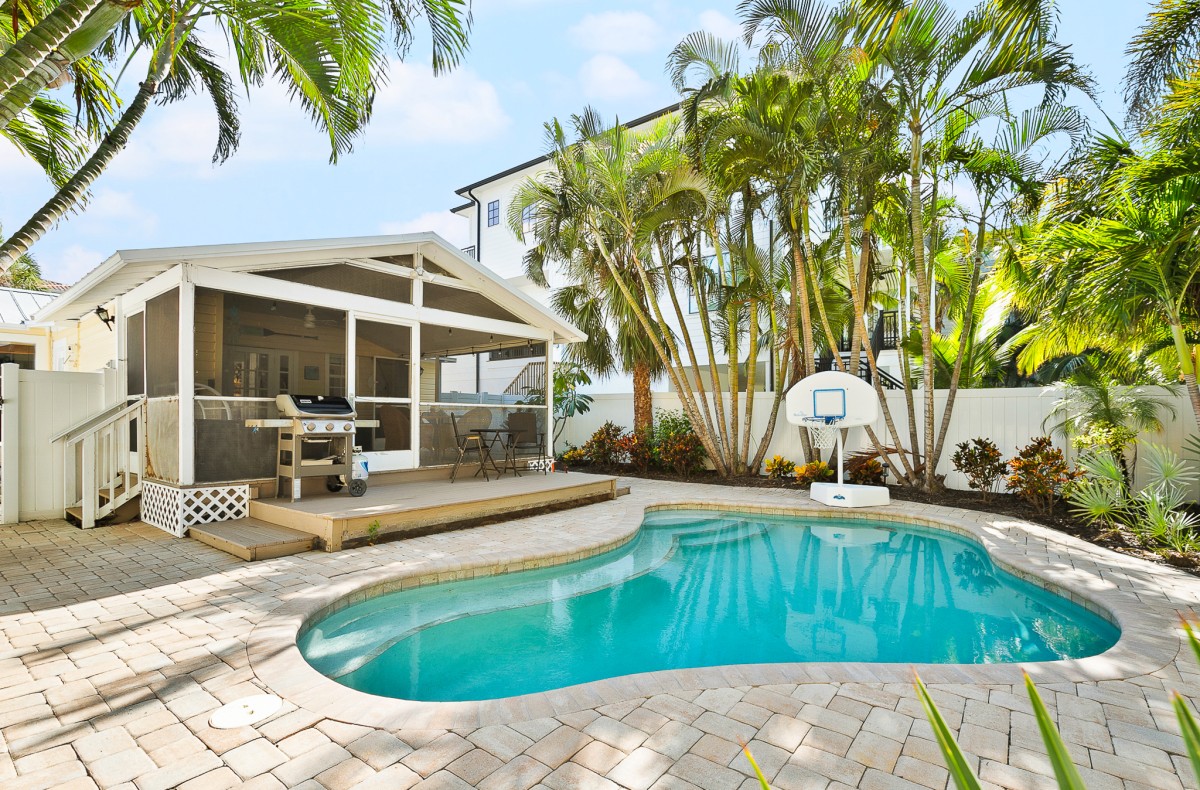 This tropical backyard features a private swimming pool, a built-in grill, and lush palm landscaping—perfect for relaxing outdoor meals after a beach day.