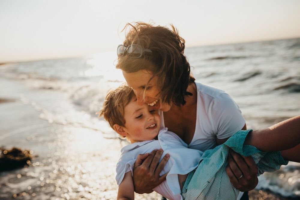 woman holding kid by ocean